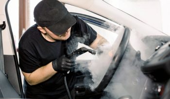 Car detailing, steam cleaning concept. Handsome man in black t-shirt and cap, worker of car wash center, cleaning car interior with hot steam cleaner. Car detailing concept.